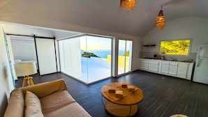 Un salon moderne avec un canapé, une table basse en bois et une vue sur la mer grâce à de grandes portes coulissantes.