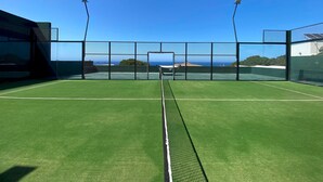 Un court de tennis en plein air offrant une vue dégagée sur l’océan et une île lointaine.
