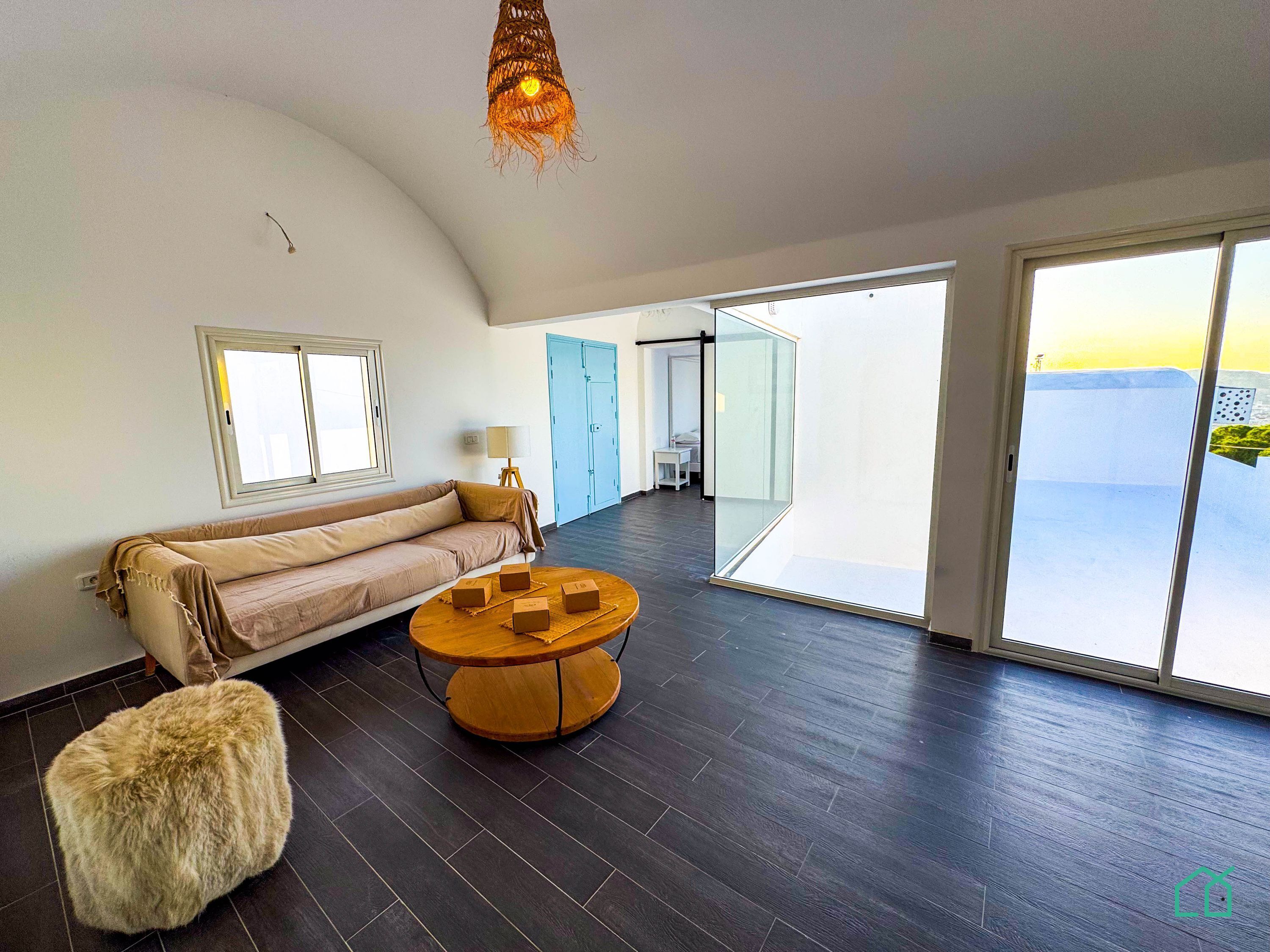 Une pièce spacieuse avec un plafond voûté, un canapé, une table ronde en bois et un pouf recouvert de fourrure.
