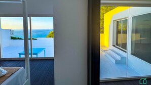 Une chambre moderne dotée d’une grande fenêtre donnant sur un balcon avec vue sur la mer.