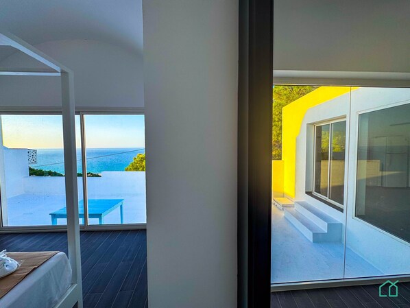 A modern room with a large window overlooking a balcony with a view of the sea. - Padel Resort 2bd Apt (Raf Raf)