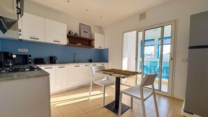 Una cucina moderna con mobili bianchi, piano cottura a gas, forno a microonde e macchina da caffè. C'è un tavolo da pranzo con sedie e vista su un balcone tramite una porta vetrata.