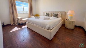Habitación de hotel con una cama grande, una mesita de noche con lámpara, una ventana con cortinas y vistas a la ciudad.