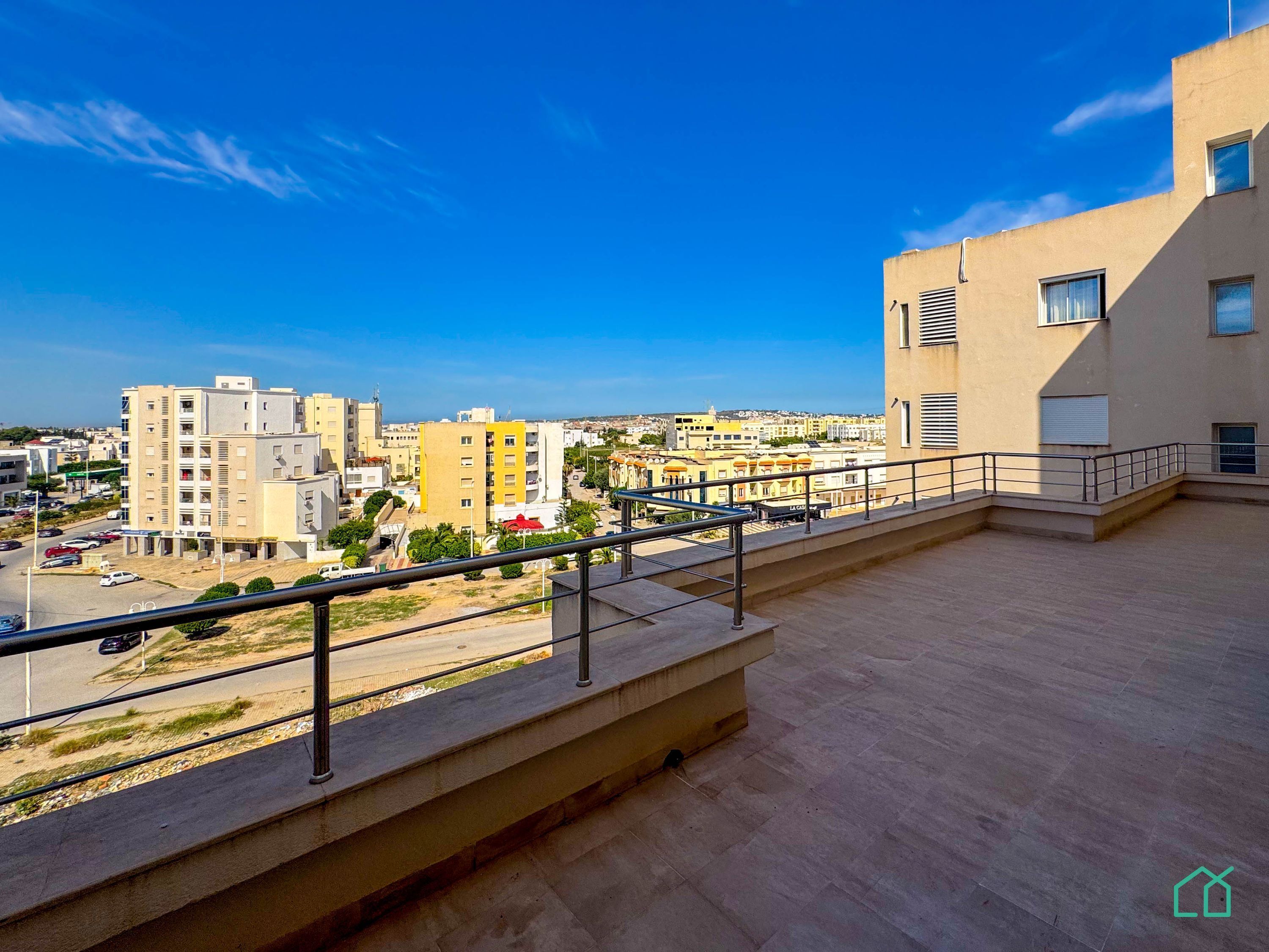 A rooftop terrace with a view of a cityscape, featuring a mix of residential buildings and a clear blue sky.