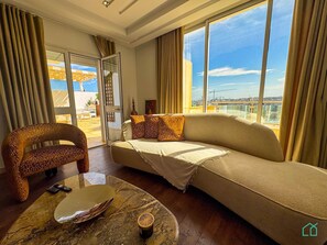 Una sala de estar moderna con un sofá, un sillón estampado, una mesa de centro de mármol y vistas de la ciudad a través de grandes ventanales.