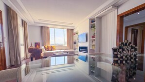 Una sala de estar moderna con una mesa de centro de vidrio, un sofá con cojines estampados, un televisor de pantalla plana y una estantería.
