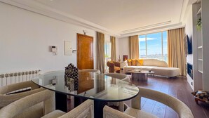 Una sala de estar moderna con una mesa de centro de vidrio, sofás color beige y vistas a la ciudad.