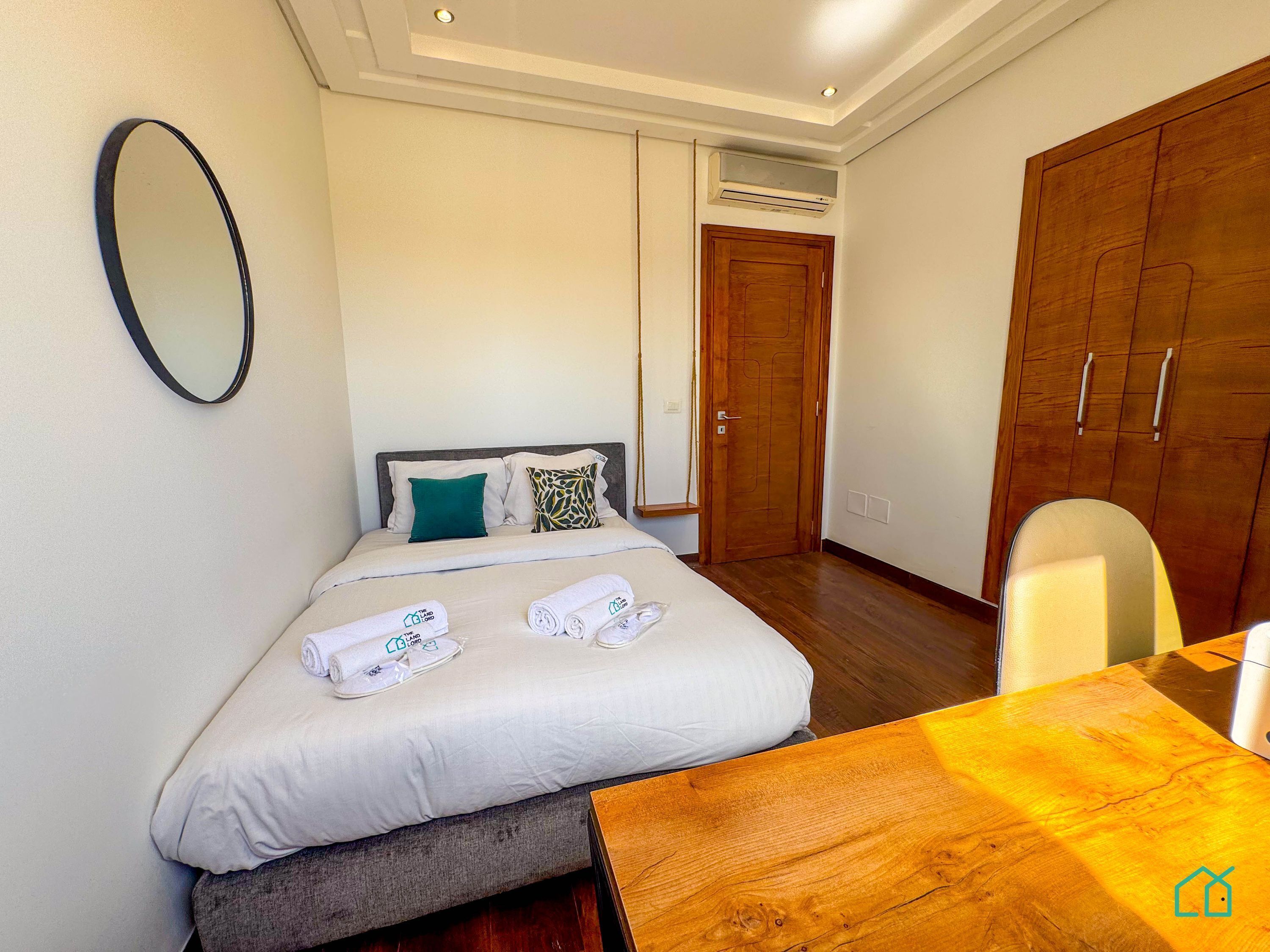 A hotel room with a bed, a wooden table, a mirror, and a wardrobe.