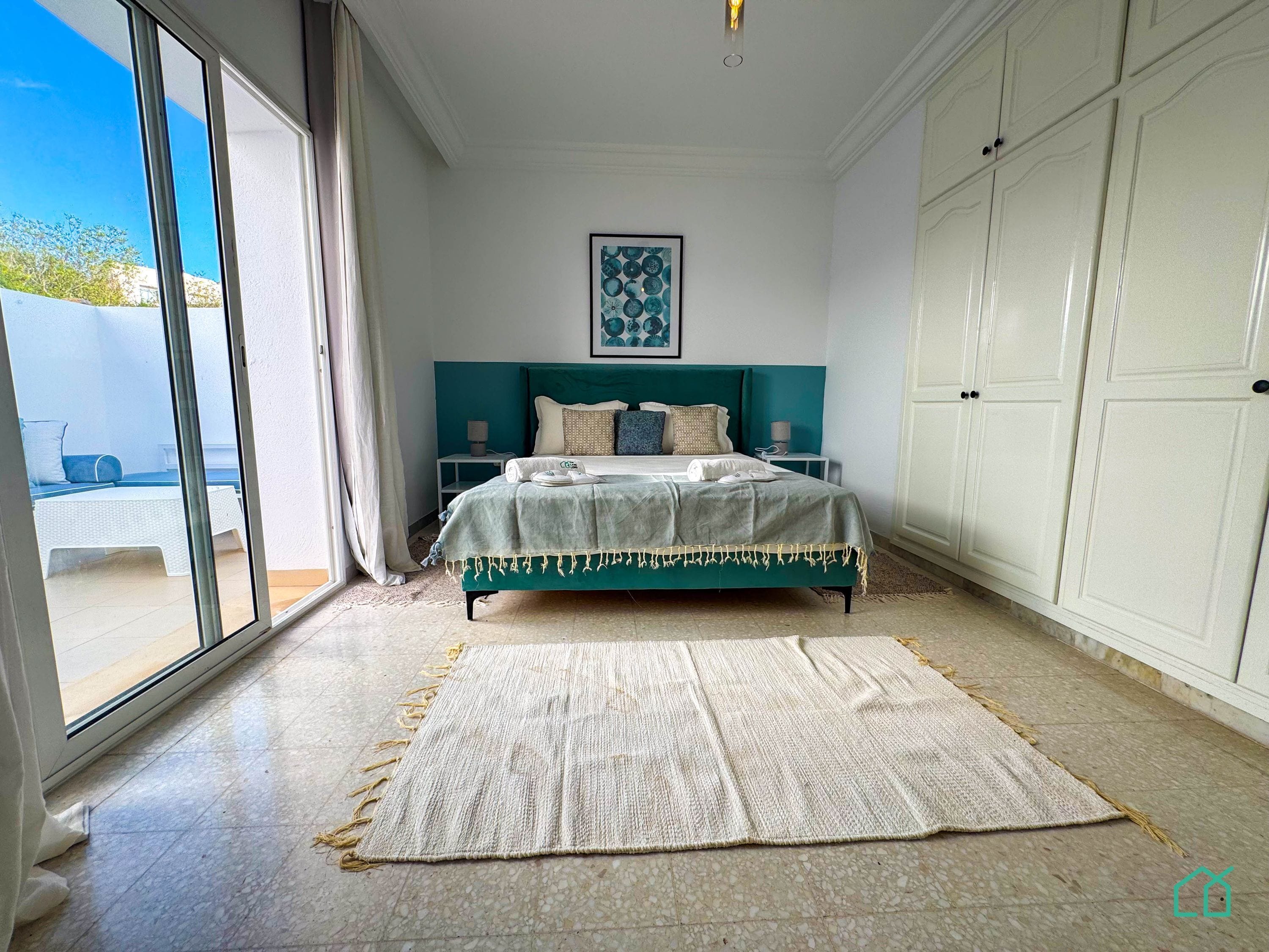 A bedroom with a bed, a large window, and a view of the outdoors.