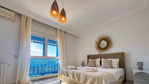 A bedroom with a large bed, a window with blue mesh, a ceiling light fixture, and a wall-mounted mirror. - Coste Sidi Bou Said A4 Cozyand Central (Sidi Bou Said)