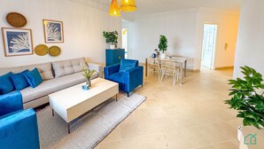 A modern living room with a sofa, blue armchairs, a coffee table, and a dining area with a table and chairs. - Coste Sidi Bou Said A4 Cozyand Central (Sidi Bou Said)