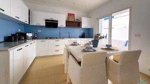 A modern kitchen with white cabinets, a black stove, and a dining area with wicker chairs and a table set for two. - Coste Sidi Bou Said A4 Cozyand Central (Sidi Bou Said)