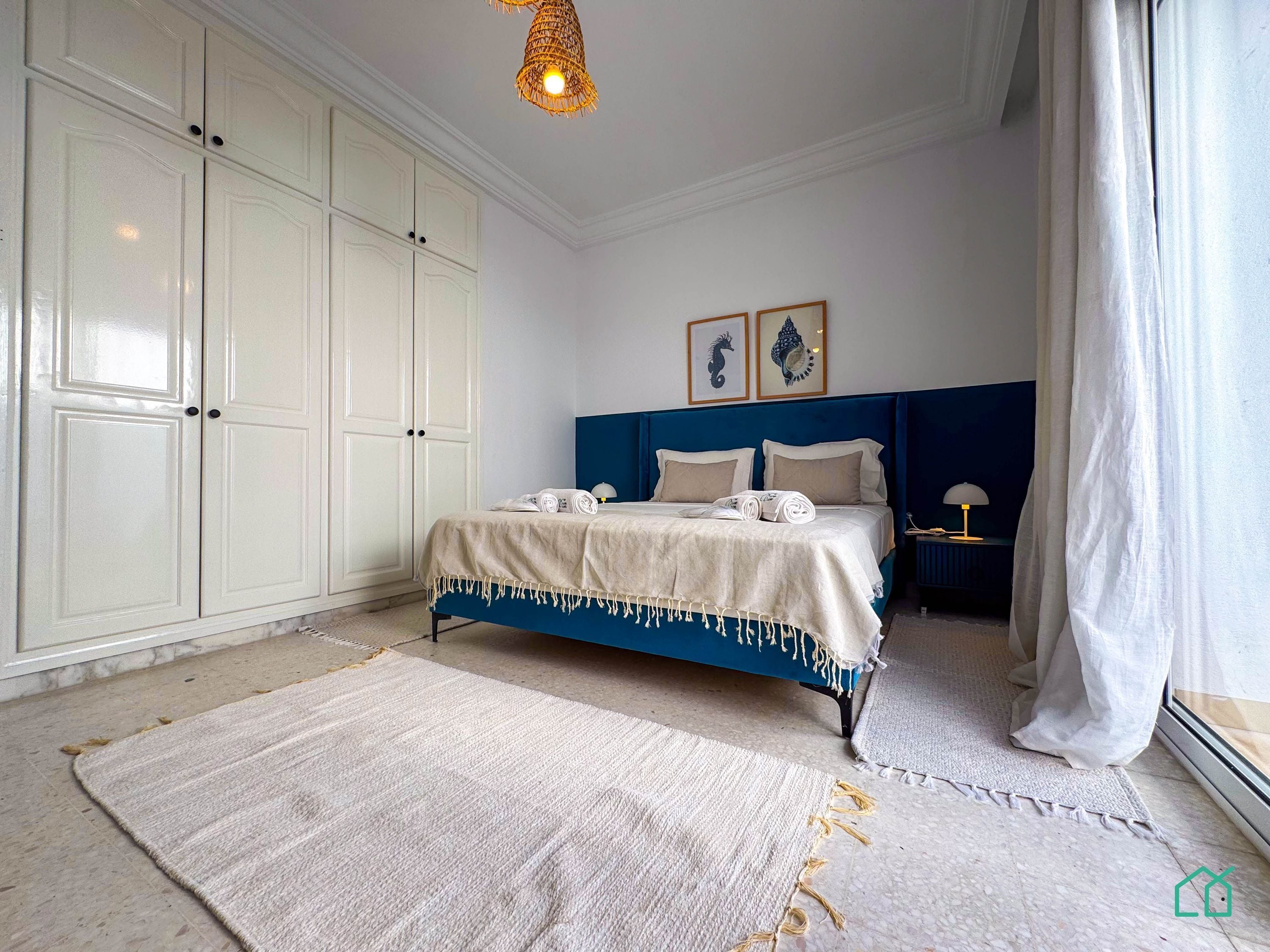 A bedroom with a bed, white wardrobe, and a large window with curtains.