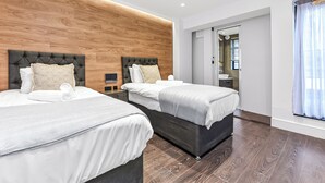 A modern hotel room with two beds, wooden headboards, and a large window with curtains. - Luxury Abode: 5-Bed Haven Ideal for Big Groups! (London)