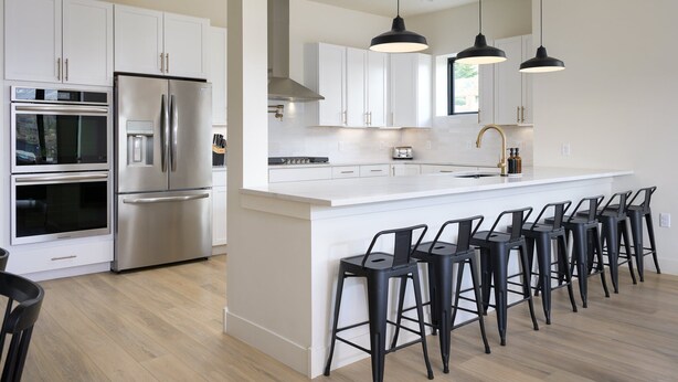 Una cocina moderna con armarios blancos, electrodomésticos de acero inoxidable y taburetes negros.