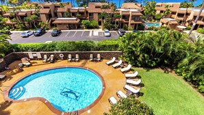 A resort with a swimming pool surrounded by lounge chairs, a parking area, and a view of the ocean. - In the Center of It all, walkable Kihei comfort (Kihei)