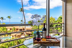 Ein Balkon mit Glastisch, einer Weinflasche, einem Weinglas mit Rotwein, einer Platte mit Käse und Crackern sowie einer Vase mit weißen Blumen.