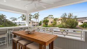 A covered patio with a wooden table and chairs, a white railing, and a view of residential houses and greenery. - Dog friendly Paradise, 1-2B Bagnall Ave - water views, air con, Wi-Fi (Salamander Bay)