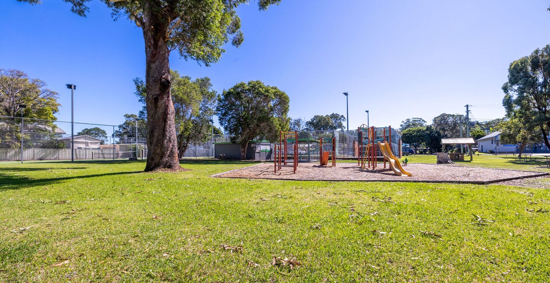 A playground with a slide and climbing structures, surrounded by a fenced area and trees.