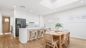 A modern kitchen with a central island, wooden bar stools, and a dining table with woven placemats. - Dog friendly Paradise, 1-2B Bagnall Ave - water views, air con, Wi-Fi (Salamander Bay)