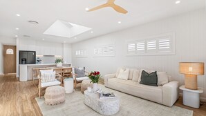 A modern living room with a sofa, coffee table, and chairs, a kitchen area with white cabinetry, and a dining space with a table and chairs. - Dog friendly Paradise, 1-2B Bagnall Ave - water views, air con, Wi-Fi (Salamander Bay)