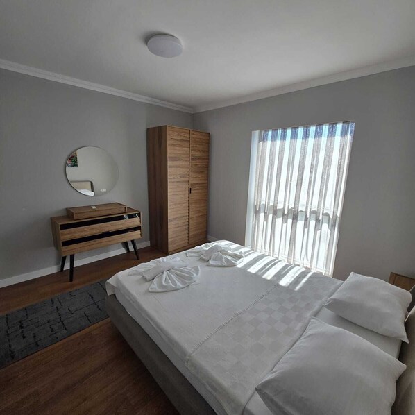 Un dormitorio con cama, armario de madera, espejo redondo y ventana con persianas verticales.