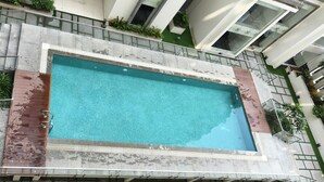 Una piscina rettangolare con superficie d'acqua cristallina e blu, circondata da un solarium in pietra e una scala metallica.
