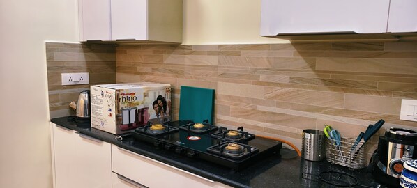 A kitchen with a gas stove, a coffee maker, and a kettle. - Sakthi Holiday's Inn (Chennai)