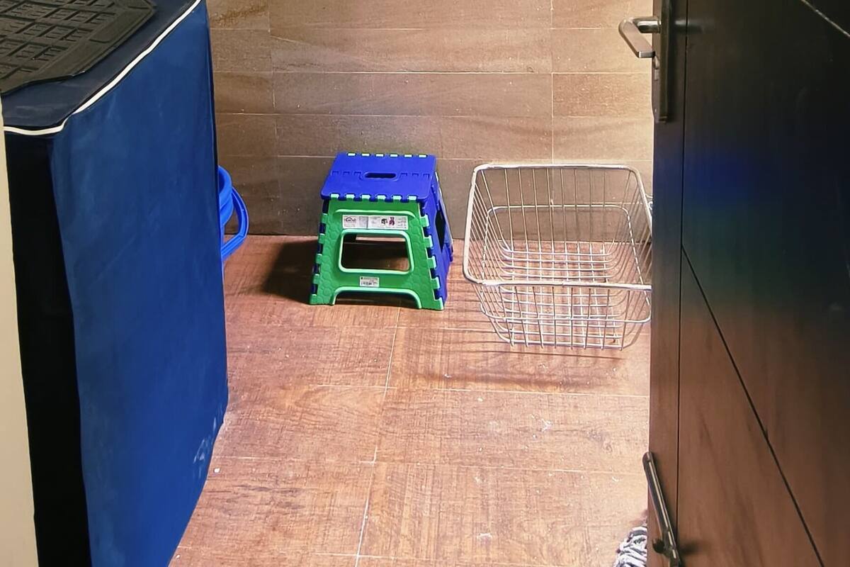 A small, narrow room with a tiled floor, a blue-covered table, a green stool, and a metal basket.