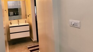 Un corridoio con un bagno dotato di lavandino, specchio e mobiletti bianchi.
