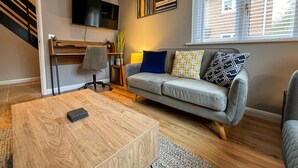 Uma sala de estar moderna com um sofá cinza, uma mesa de centro de madeira e uma TV fixada na parede.
