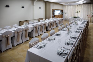 A banquet hall with long tables set for a formal event, featuring white tablecloths and chairs with beige sashes. - Árnyas Panzió Gödöllő (Gödöllő)