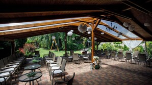 An outdoor patio area with wooden beams, tables, chairs, and hanging decorations. - Árnyas Panzió Gödöllő (Gödöllő)