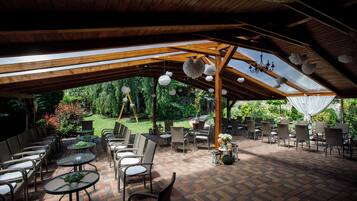 Un patio al aire libre con vigas de madera, mesas, sillas y adornos colgantes.