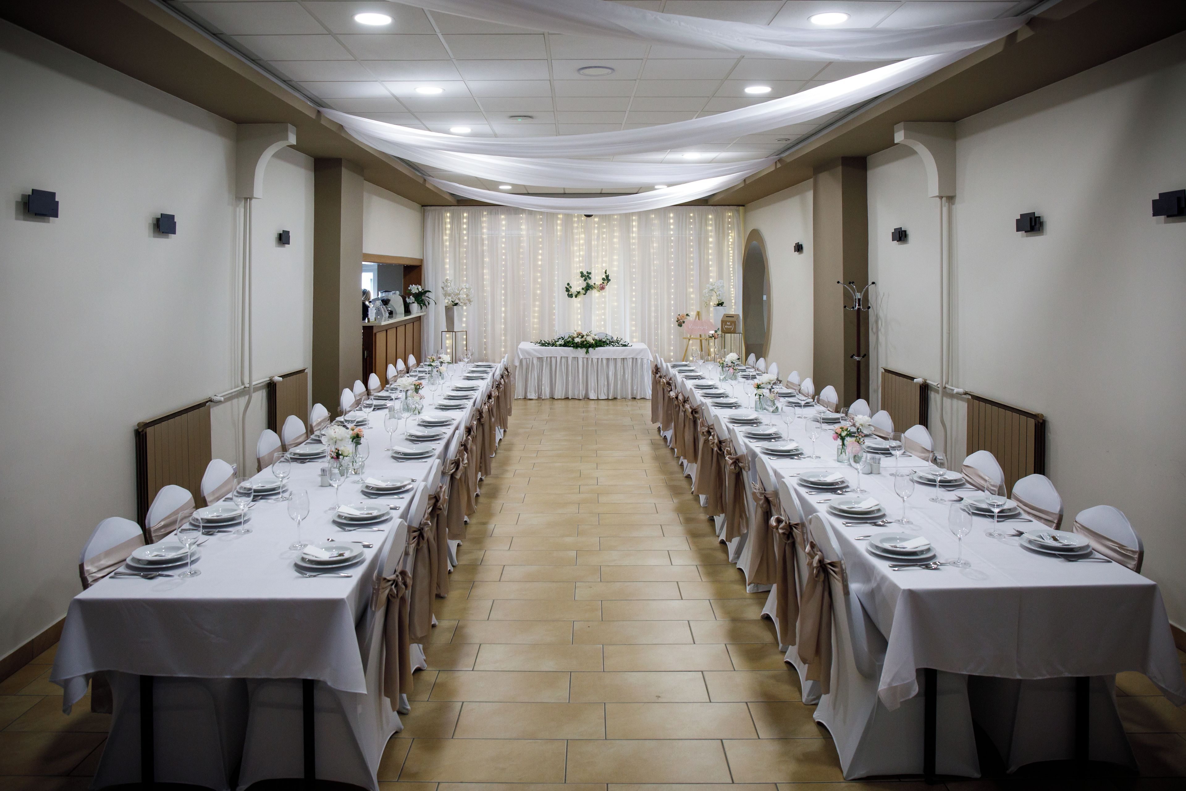 A long banquet hall with tables set for a formal event, featuring a central stage and decorative lighting.