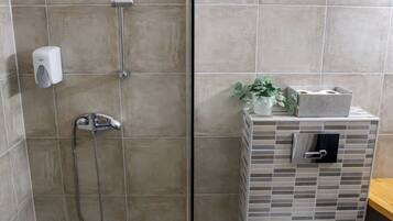 A bathroom with a glass-enclosed shower, a toilet, and a small sink area with a plant and storage box.