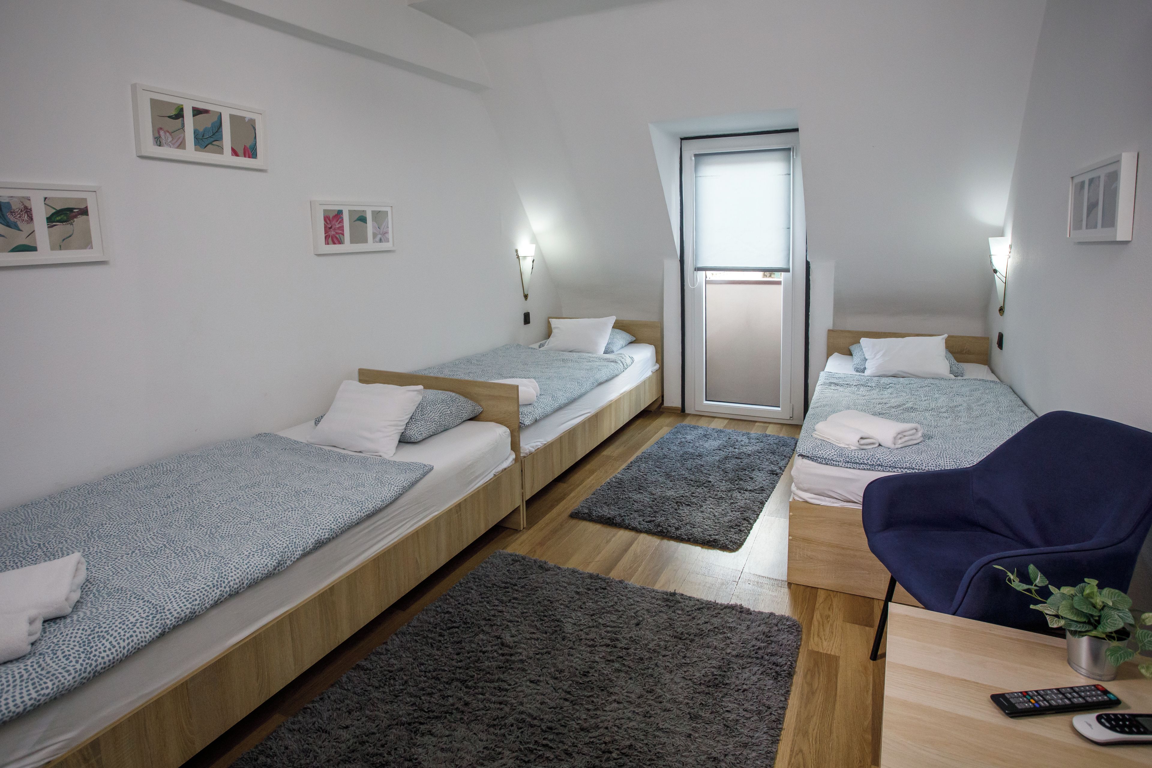 A small, modern room with three single beds, a desk with a chair, and a small potted plant.