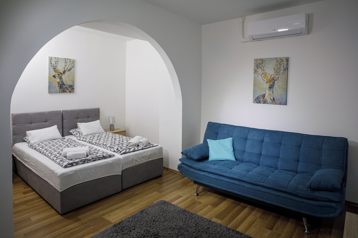 A bedroom with a bed, a blue sofa, and two wall-mounted paintings.