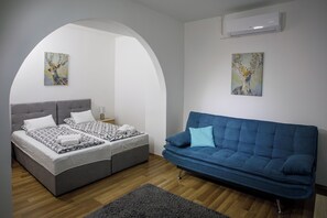 A bedroom with a bed, a blue sofa, and two wall-mounted paintings. - Árnyas Panzió Gödöllő (Gödöllő)