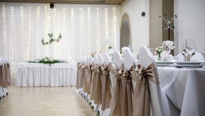 A banquet hall with rows of tables set for a formal event, featuring white tablecloths and chairs with beige sashes. - Árnyas Panzió Gödöllő (Gödöllő)