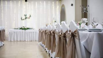 A banquet hall with rows of tables set for a formal event, featuring white tablecloths and chairs with beige sashes.