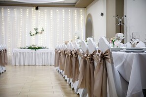 A banquet hall with rows of tables set for a formal event, featuring white tablecloths and chairs with beige sashes. - Árnyas Panzió Gödöllő (Gödöllő)