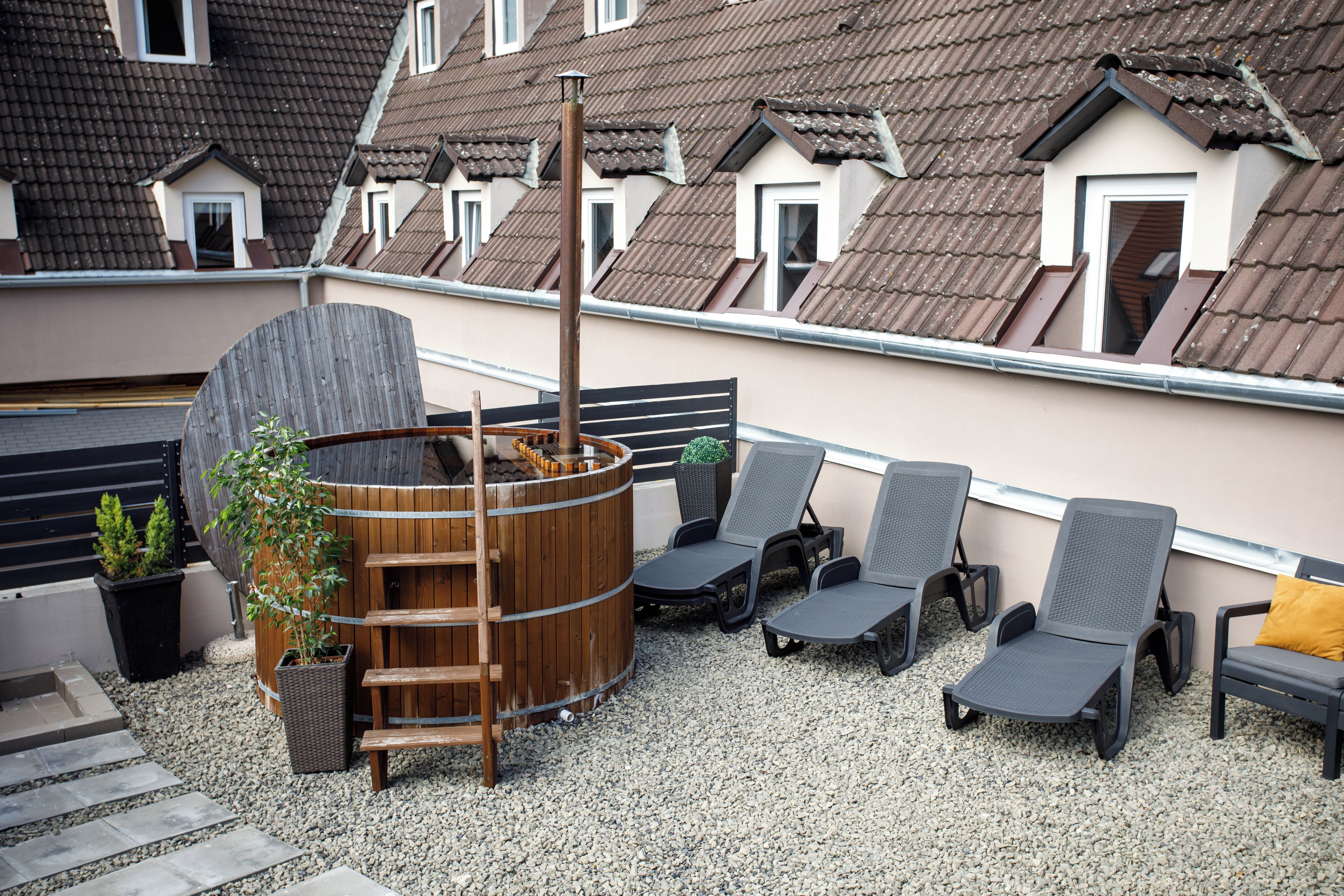 A rooftop terrace with a hot tub, lounge chairs, and potted plants.