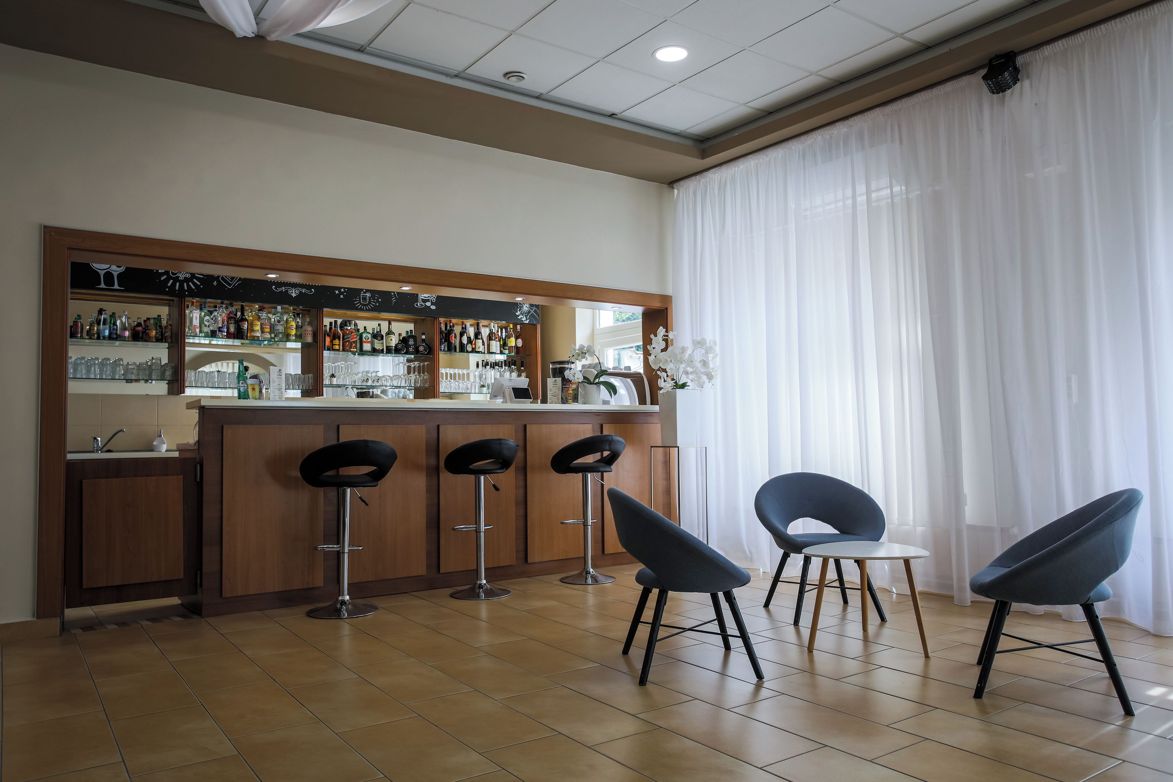 A bar area with a counter, stools, and a view of the outside through large windows.