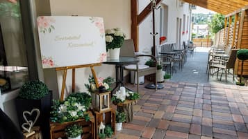 Un patio al aire libre con una pérgola de madera, suelo de ladrillo y diversas macetas con plantas y flores.