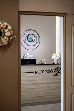 A reception area with a wooden reception desk, a wall-mounted mirror, and a floral arrangement. - Árnyas Panzió Gödöllő (Gödöllő)