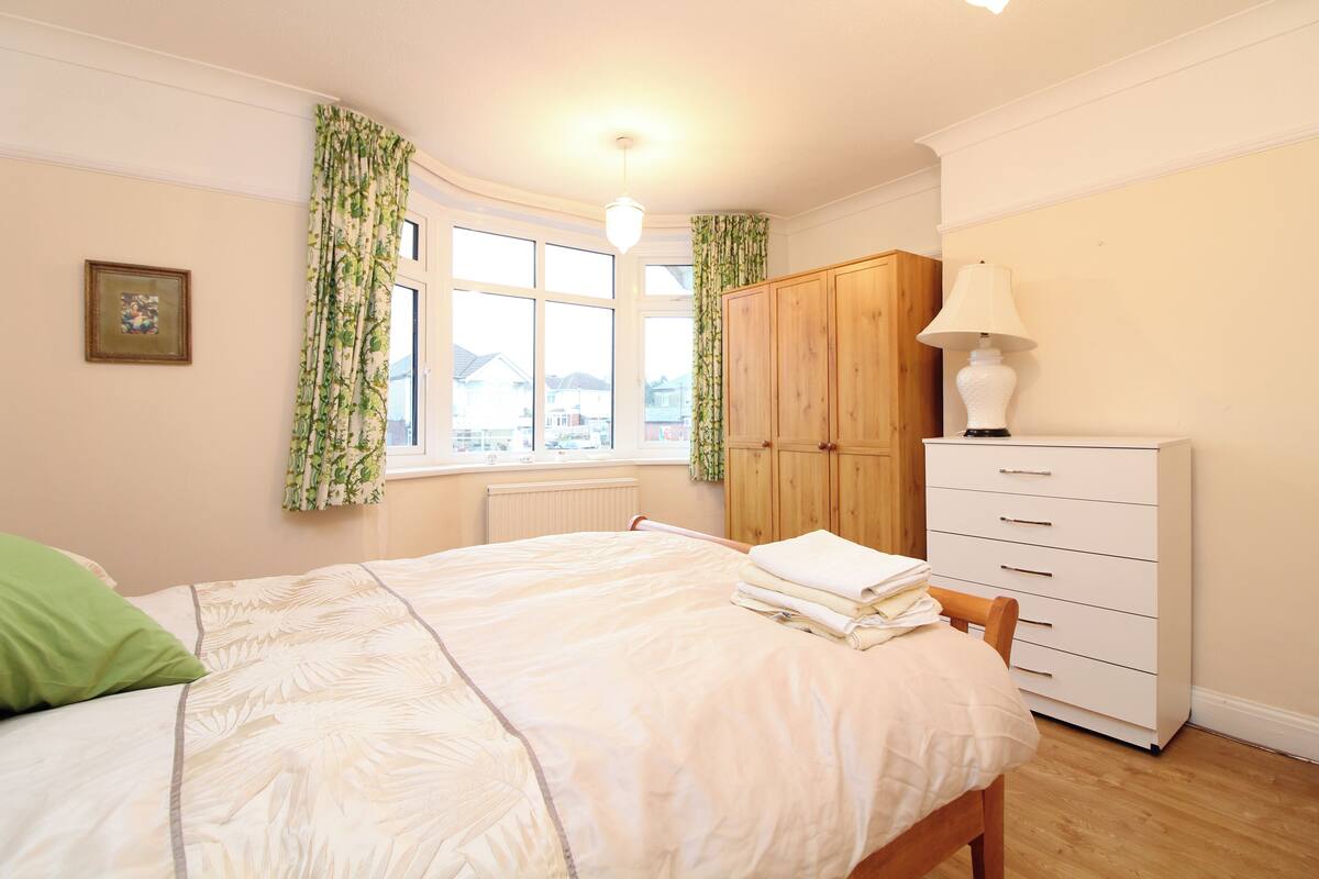 A bedroom with a bed, a dresser, a window with curtains, and a radiator.
