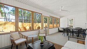 Une vaste terrasse dotée de grandes fenêtres, de fauteuils en osier, d’une table ronde et d’un ventilateur de plafond.