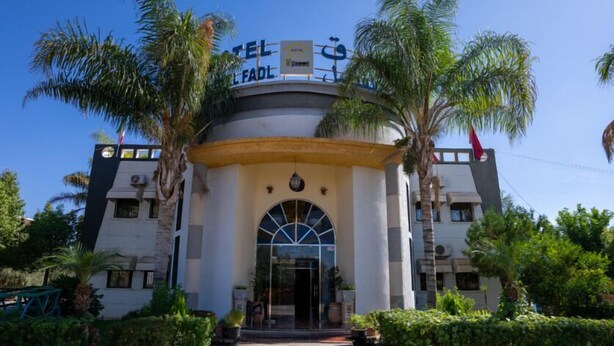 Entrada de hotel con un arco central, palmeras y un cielo azul despejado.