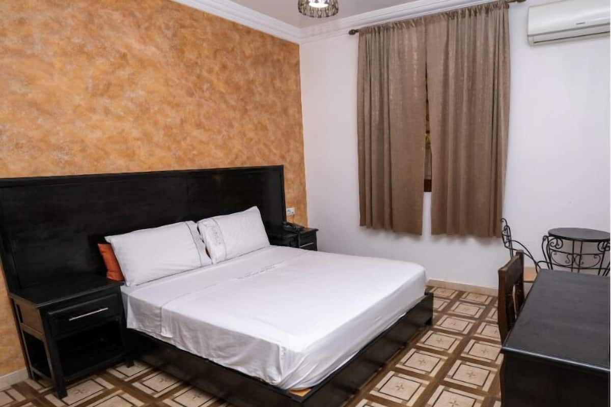 Una habitación de hotel con una cama, una mesita de noche, un escritorio y una ventana con cortinas.